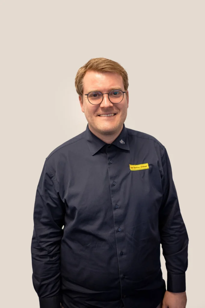 Portræt af en smilende Ivan Bastrup Jakobsen, direktør for Entreprenør IvanBJ, iført mørkeblå skjorte og briller.