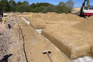 Udgravning af fundamentgrøfter til nybyggeri, med delvist støbte fundamenter og gravemaskine på byggepladsen.